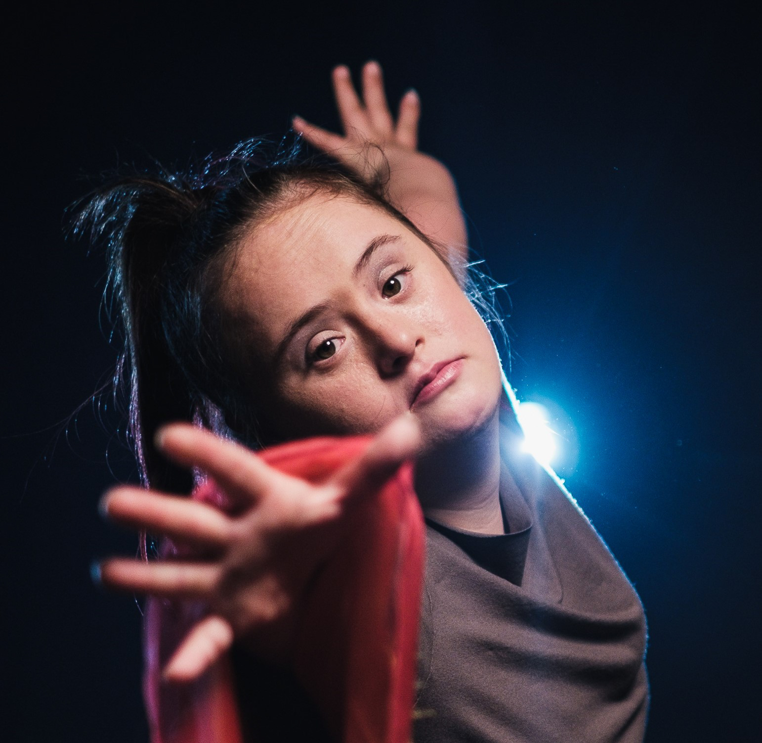 A dancer in front of a dark background looks directly into the camera and ‘reaches’ for the viewer with her hand