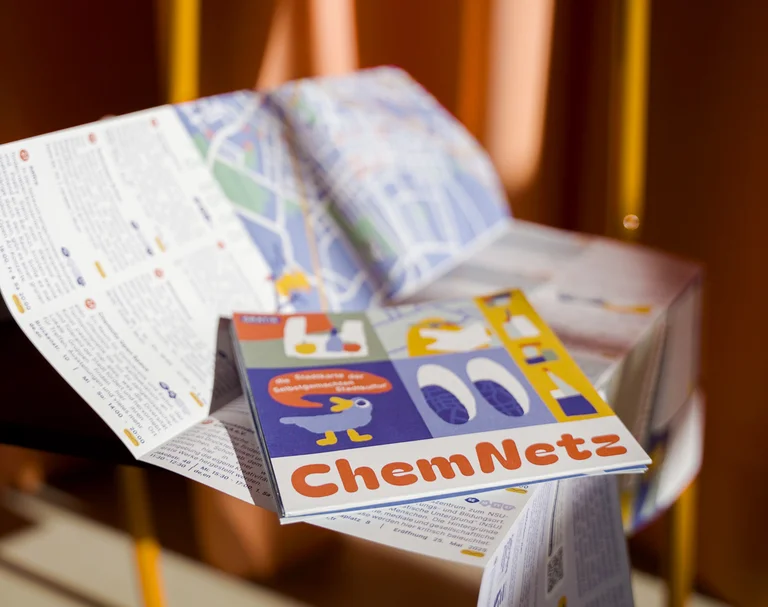 Auf einem Stuhl liegt eine aufgefaltete Broschüre mit Text und einer Karte von Chemnitz.