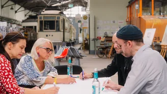 vier Personen sitzen an einem Tisch mit einem Plakat