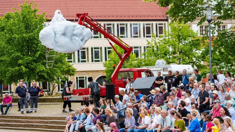 eine große Menschenmenge schaut zu einer an einem Kran befestigten Wolke hinauf