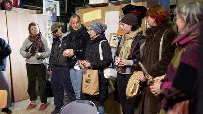 Frauen stehen in einer Werkstatt und haben unterschiedliche Gegenstände in der Hand