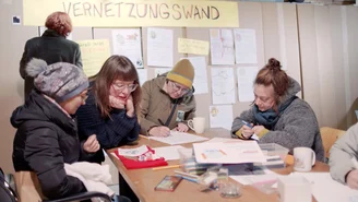mehrere Frauen sitzen um einen Tisch und arbeiten an Plakaten