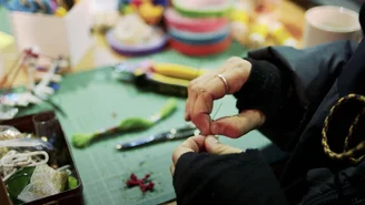 Hands of a person working at a craft table with various materials and tools.