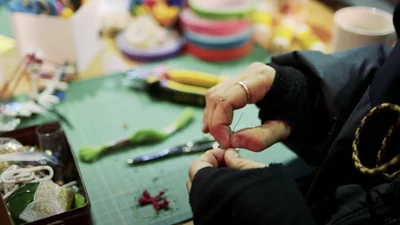 Hände einer Person, die an einem Basteltisch mit verschiedenen Materialien und Werkzeugen arbeitet.