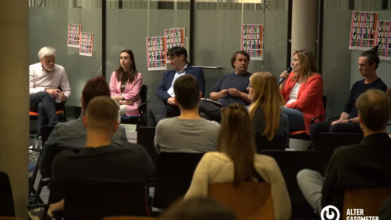 Eine Gruppe von Menschen sitzt im Kreis, eine Person spricht in ein Mikrofon.