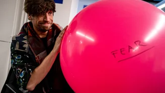 a large colourful balloon with ‘FEAR’ written on it in sharpie, a person holding it as if he had just blown it up