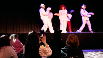 Jugendliche im Publikum filmen und betrachten Tänzerinnen auf der Bühne.