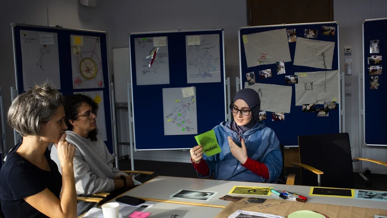 Three women are sitting at a table talking about the project.