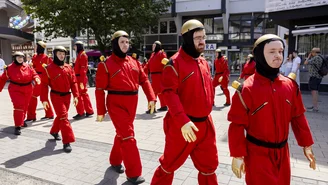 People dressed up as robots walk in a row with their arms and legs outstretched