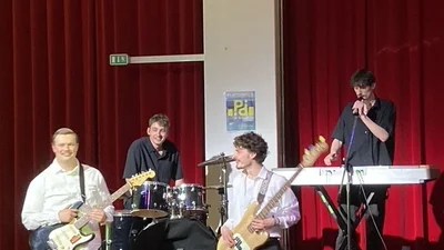 Eine Band aus vier jungen Männern steht auf einer kleinen Bühne und spielt am Abend der Veranstaltung.