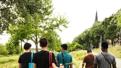 Eine Gruppe von Jugendlichen läuft durch die Natur mit Kameras und einem Eroller.