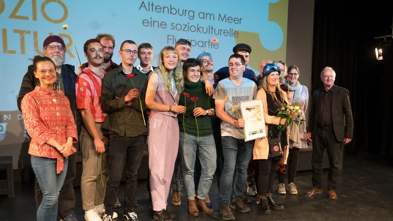 eine Gruppe von jungen Menschen auf der Bühne mit Blumen und einer Urkunde in den Händen