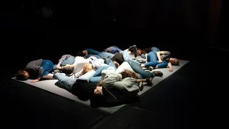 in einem dunklen Raum liegen mehrere Personen auf einer kleinen Bühne