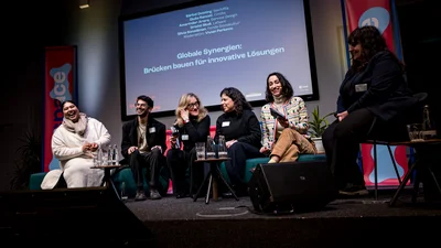 Eine Gruppe von Personen diskutiert auf der Bühne zum Thema Globale Synergien