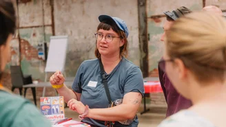 Eine Person erklärt ihr Projekt an einem Stehtisch mehreren Personen.