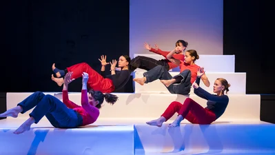 Fünf junge Frauen während einer Tanzperformance auf einer Bühne bestehend aus großen Treppenstufen.