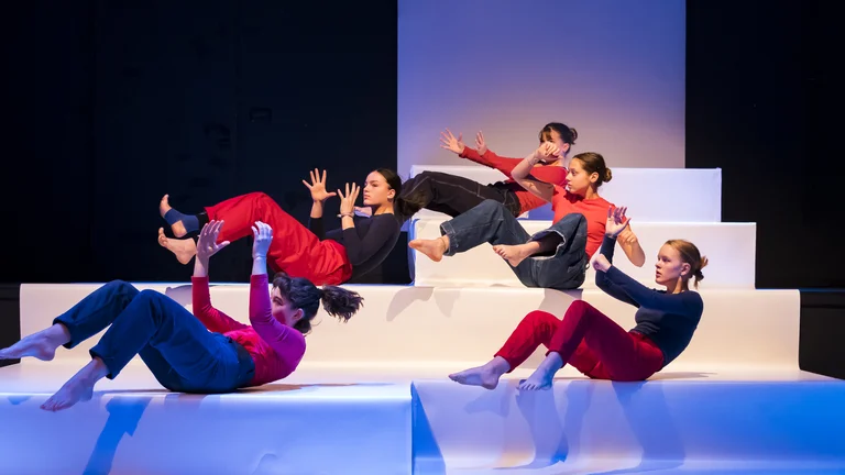Fünf junge Frauen während einer Tanzperformance auf einer Bühne bestehend aus großen Treppenstufen.