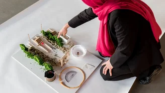 Draufsicht auf eine Person mit Hijab, die mit dem Finger auf ein Miniaturmodell zeigt.