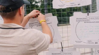 eine Person hängt den Deckel eines Pizzakartons an ein Gitter. Darauf steht die Frage Wie kann Kultur in deinem Ort die Gemeinschaft stärken?