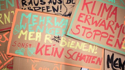 Kartonschilder, auf denen mit bunter Farbe in großen Buchstaben verschiedene Sprüche stehen, z.B. Klimawandel stoppen, mehr Bienen.