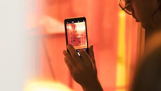 Eine Person fotografiert mit dem Smartphone eine Installation hinter einer Scheibe.
