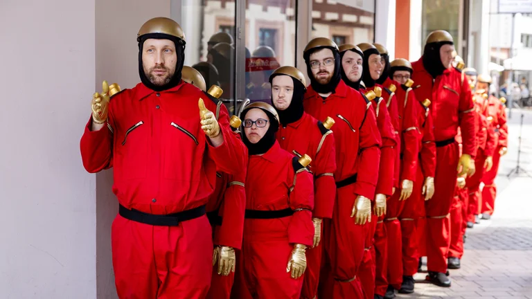 an inclusive dance group dressed as robots lined up one behind the other in a street