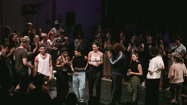 Several young people stand on a stage, each with a rose in their hand, clapping their hands