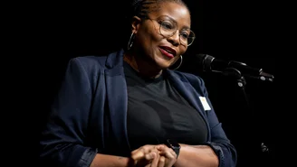 a woman stands in front of a microphone and gesticulates with her hands
