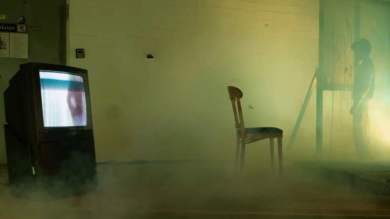 ein alter Fernseher und ein Stuhl umgeben von Nebel in einem leeren Raum.
