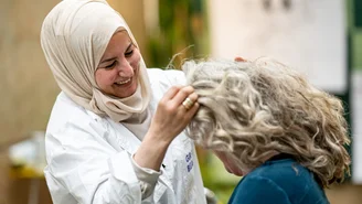 a smiling woman styles another woman's curly hair or massages her head