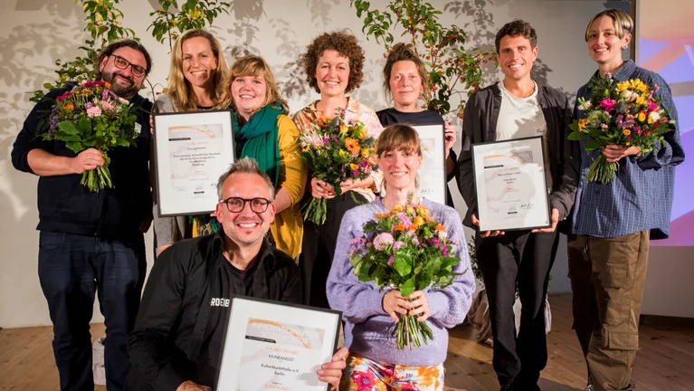 Gruppenfoto der Preisträger und Preisträgerinnen mit Urkunden und Blumen