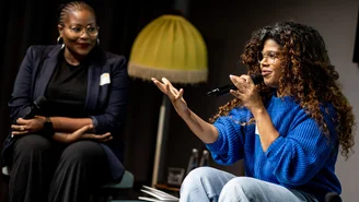 two women on stage, a floor lamp in the background