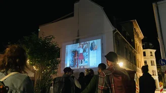 Personen schauen ein Video, das im Großformat auf eine Hauswand projiziert wird.